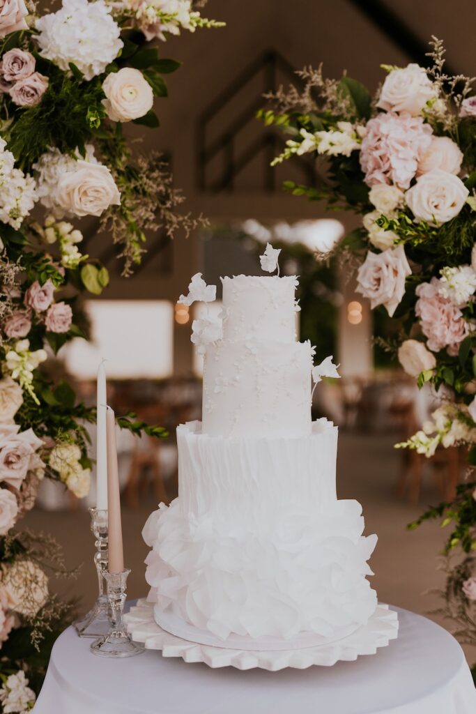 White tiered wedding cake displayed beneath floral arch at Dallas wedding venue