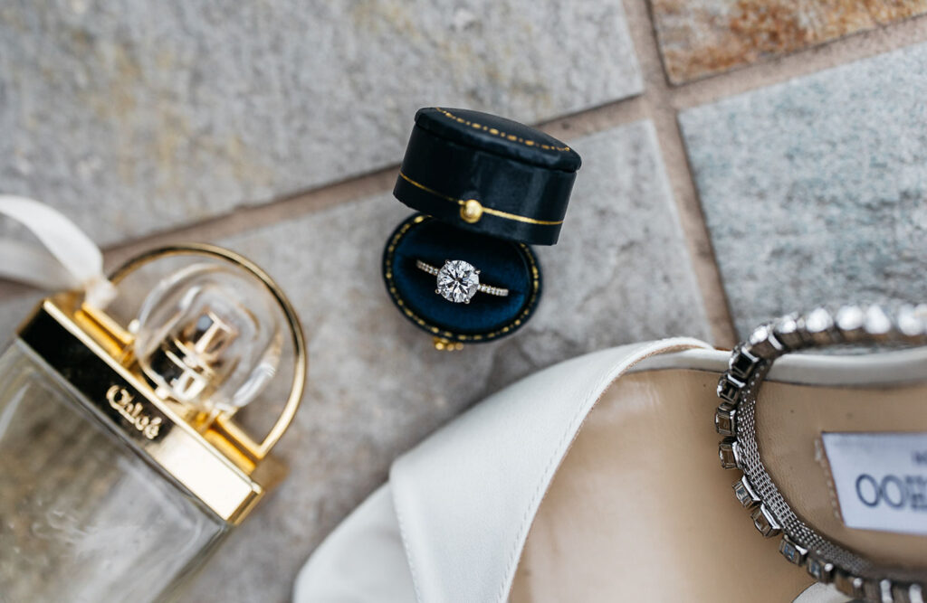 Flat lay of wedding details including engagement ring box, heels, and accessories
