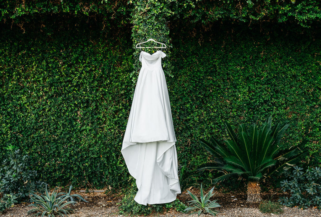 Wedding dress hanging outdoors against lush green ivy
