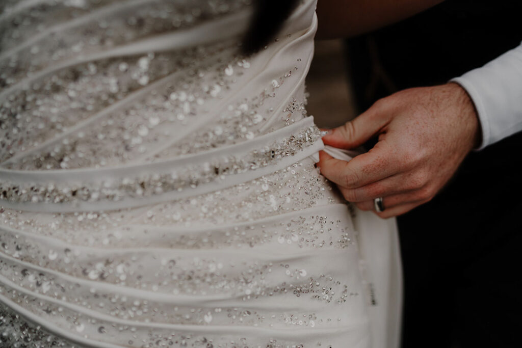 Close-up of bride’s hands adjusting beaded wedding dress
