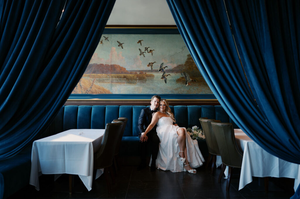 Bride seated alone in a blue velvet booth during wedding portraits