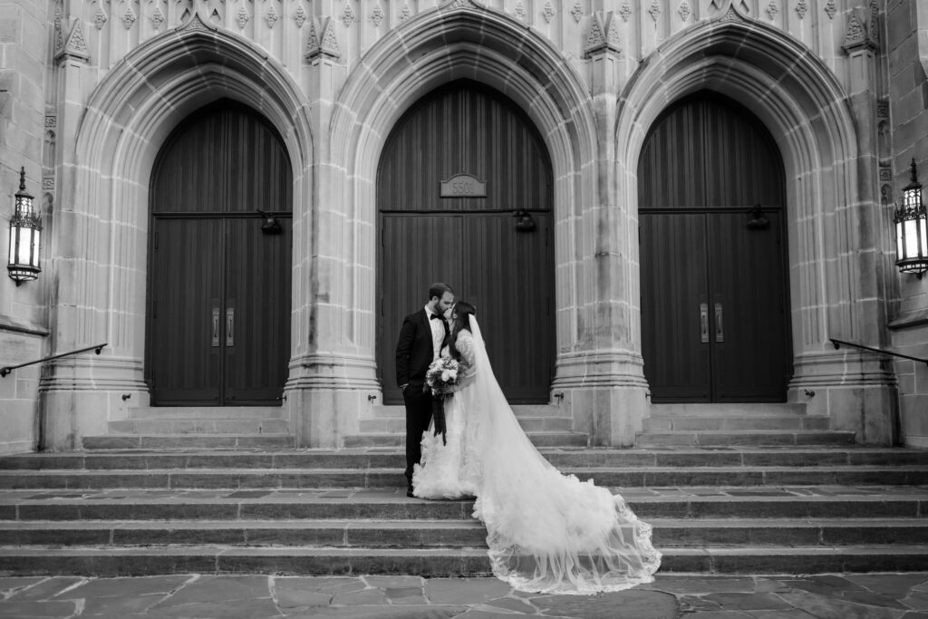 Black and white photo of bride and groom standing together on church steps