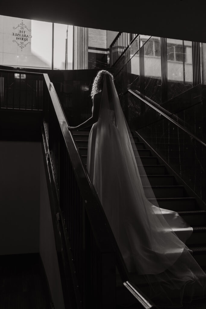 Bride ascending a staircase with her wedding veil flowing behind her