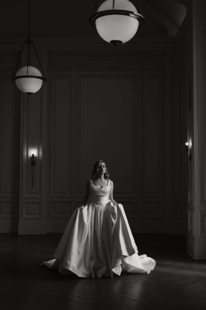 Bride standing alone in a softly lit room wearing a wedding gown