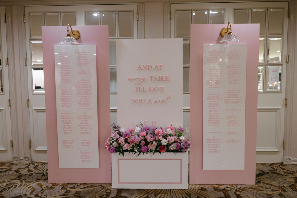 Wedding reception seating chart with large pink boards and gold sconces at The Adolphus in Dallas