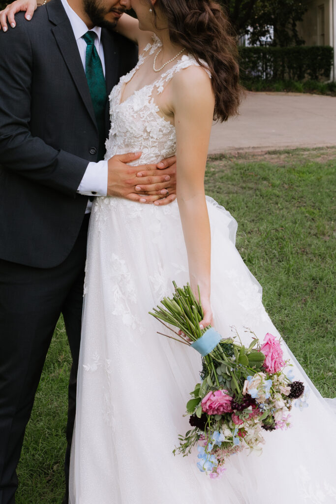 Bride holding bouquet of flowers and embracing groom at Arlington Hall in Dallas