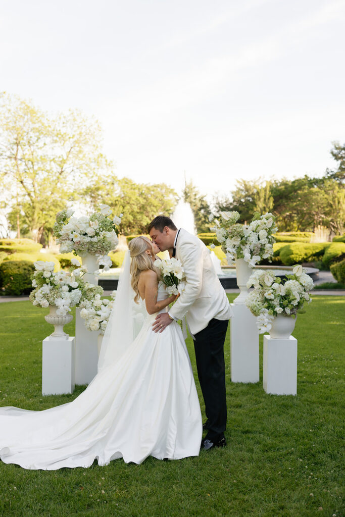 Bride and groom kissing in front of white floral arrangements at Texas Discovery Gardens