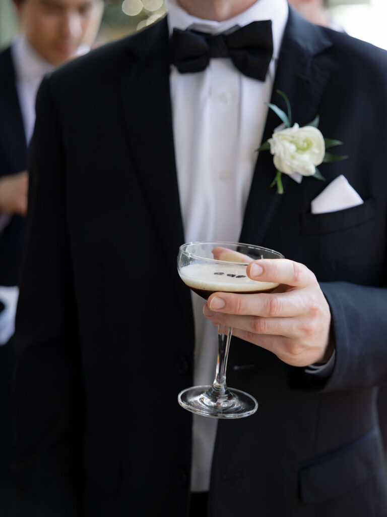 Close up of a groom in a black tux holding an espresso martini
