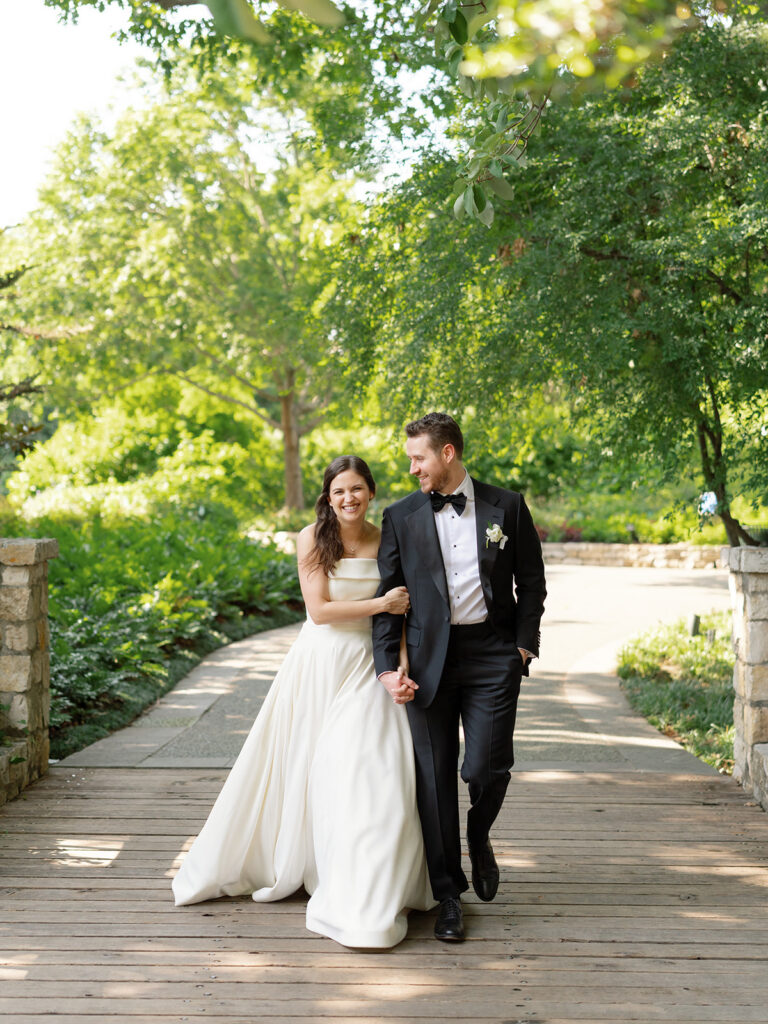 Bride and groom laughing and walking outside down a pathway under trees