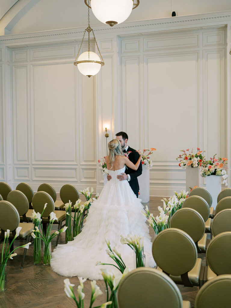 Bride and groom kissing in a ceremony space with the aisle lined with white lilies leading up to orange and white floral arrangements