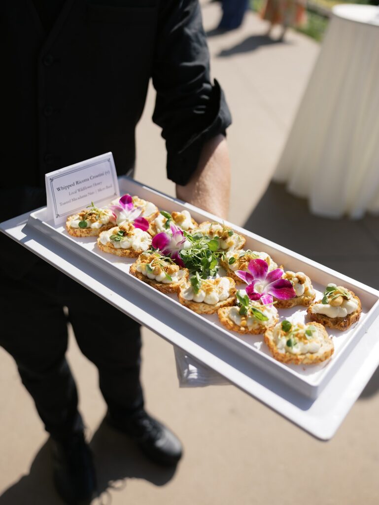 Waiter at wedding holding white tray of whipped ricotta crostini